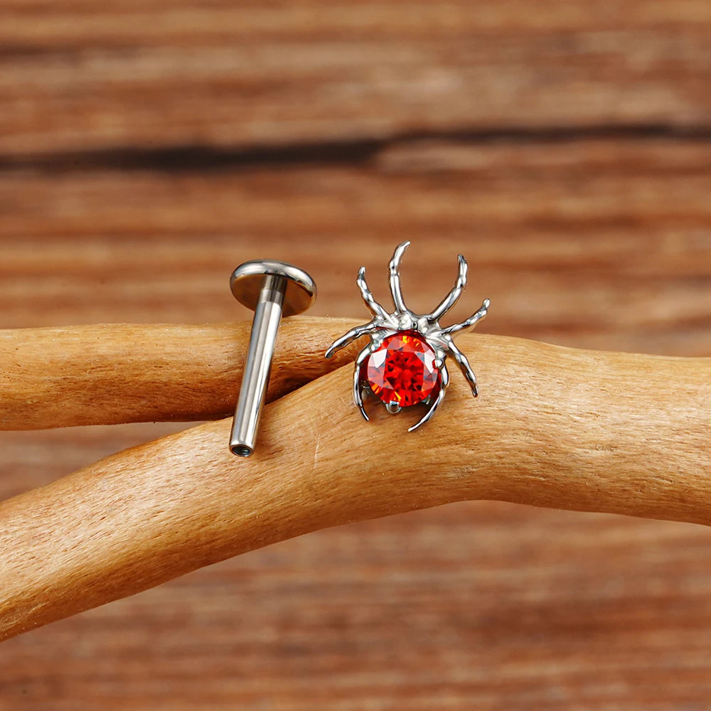 Spinnen-Piercing mit einem roten Edelstein in Schwarz, Silber und Gold. Rechter Halloween-Piercing-Schmuck, Ohrstecker aus Titan