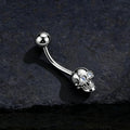 Silver skull-themed belly button ring on a dark textured background